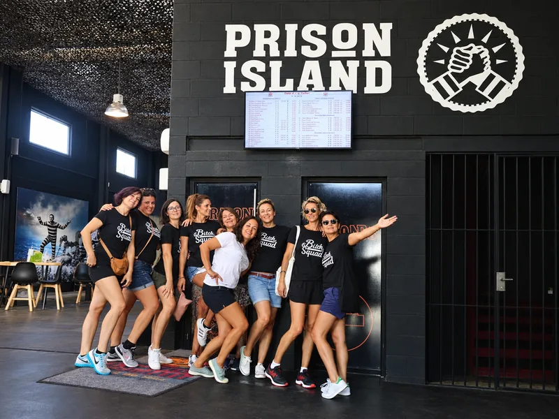 Un groupe d'amis en tee-shirts assortis pose devant l'enseigne Prison Island